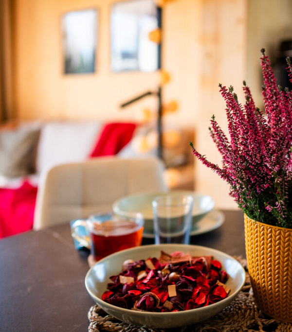 Wohnzimmer im Holzdesign mit einer weißen Couch im Hintergrund. Im Vordergrund sieht man einen Tisch mit einer Pflanze und einer Schüssel mit roter Dekoration.